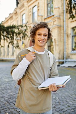 Handsome student stands in a lively courtyard, ready to unleash creativity with his sketchbook. clipart