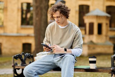 Şık bir genç adam rahat bir şekilde dışarıda oturuyor, akıllı telefonuna dalmış..