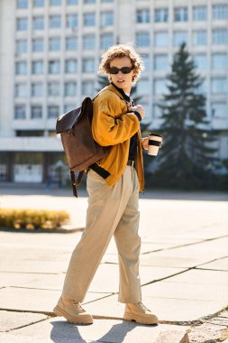 Moda kıyafetleri içinde gezen genç adam kentin dışında kahvesini yudumluyor..