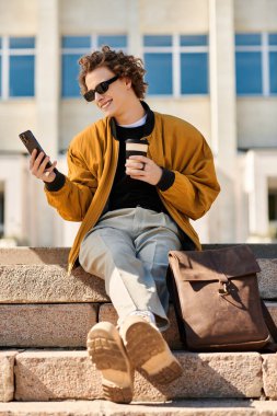 Modayı takip eden genç bir adam taştan basamaklarda oturur, kahvesini yudumlar ve güpegündüz telefonuna güler..