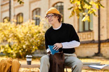 Şık giyinmiş genç bir adam bankta oturur, kahvesini yudumlar ve dışarıda ders çalışır..