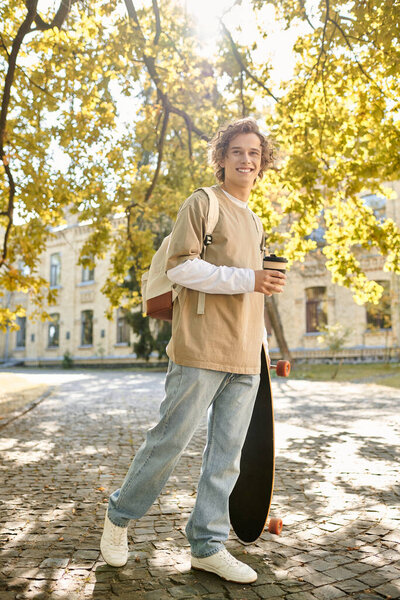 Handsome student walks along cobblestone path sipping coffee, basking in warm sunlight under trees.