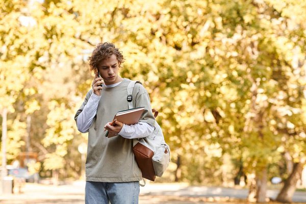 A handsome young man with curly hair talks on the phone amid fall foliage.