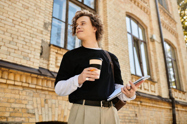 Confident young man holds a cup of coffee and a notebook, taking in the vibrant campus atmosphere.