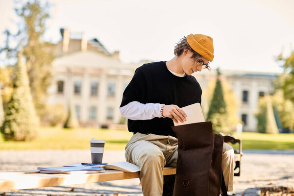Young man sits on a bench at a beautiful campus, focused on his studies with coffee at hand.
