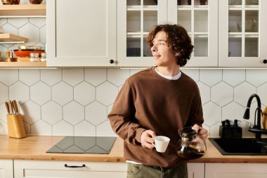 Kıvırcık saçlı bir öğrenci modern mutfağında dinleniyor ve ders arası sırasında kahvenin tadını çıkarıyor..