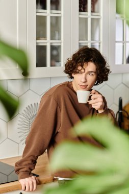 Kıvırcık saçlı genç bir adam yeşil, şık bir dairede kahvenin tadını çıkarıyor..
