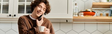Kıvırcık saçlı öğrenci telefonda konuşurken ve evde kahve içerken sıcacık gülümsüyor.
