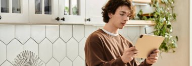 Kahverengi kazaklı genç adam şık bir şehir ortamında tabletine odaklanıyor.