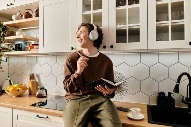 Kıvırcık saçlı öğrenci, çağdaş bir mutfakta notlar yazarken rahatlıyor..