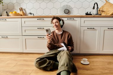 Yerde dinlenirken, genç bir adam müzik dinlerken gülümser ve notaları not alır..