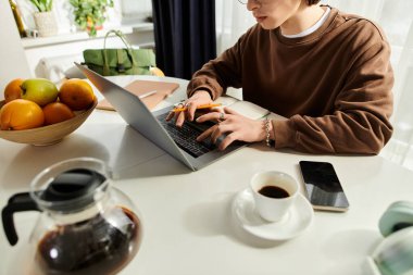 Kahverengi kazaklı genç adam şık bir dairedeki masada özenle ders çalışıyor..
