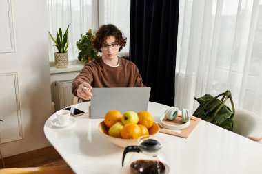 Kahverengi kazaklı genç bir adam bitkilerle dolu rahat bir dairede dizüstü bilgisayarına odaklanıyor..