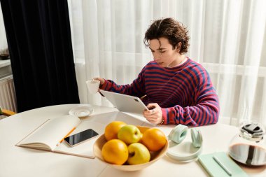 Genç bir ikili olmayan kişi, modern evlerinde tablet okurken kahveden zevk alır..