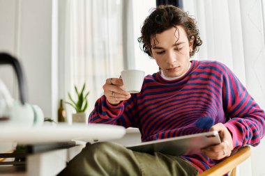 Parlak giyimli birey, şık ve modern bir yerde okurken bir içkiyle rahatlıyor..