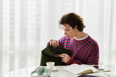 Canlı çizgili kazaklı, ikili olmayan genç bir insan rahat bir yerde çantasını karıştırıyor..