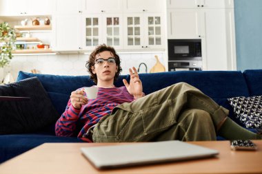 İkili olmayan genç bir insan şık bir dairede rahatça oturur ve bir fincan kahvenin tadını çıkarır..