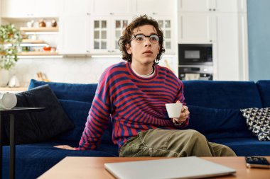 İkili oynamayan genç bir insan kanepede rahatlar, rahat bir dairede içki yudumlar..