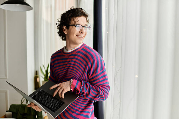 Молодой человек с вьющимися волосами улыбается, используя ноутбук в своем ярком доме.