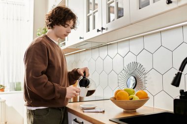 Kahverengi kazaklı kıvırcık saçlı genç adam modern mutfağına meyve dolu kahve döker..