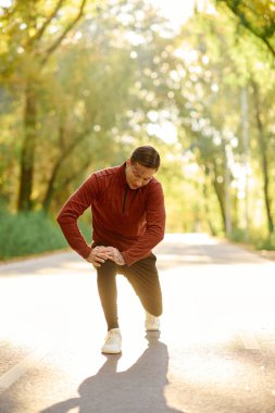 A tattooed young man kneels on a road, showing off his stylish outfit in autumn leaves. clipart