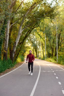 Dövmeleri olan yakışıklı bir adam, canlı sonbahar renkleriyle çevrili ağaçlık bir yolda koşuyor..