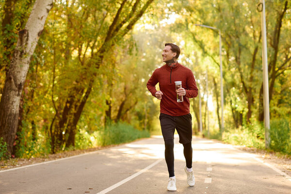 Красивый мужчина в модном костюме бегает по живописной тропинке в окружении ярких деревьев.