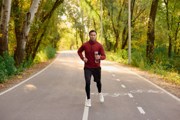 Красивый мужчина в модном наряде бежит по живописной тропинке в окружении красочной осенней листвы.