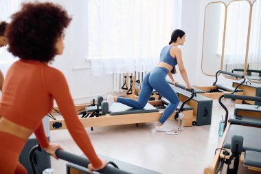Katılımcılar iyi aydınlatılmış bir stüdyoda pilates yapıyorlar, kendilerini odaklanmış egzersizlere kaptırıyorlar..