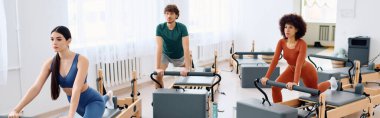 Üç katılımcı parlak, modern bir pilates stüdyosu ortamında yaptıkları egzersizlere odaklanıyor..