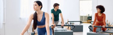Nişanlı bireyler, iyi aydınlatılmış bir pilates stüdyosunda bir ders sırasında reformcular üzerinde alıştırmalar yapıyorlar..