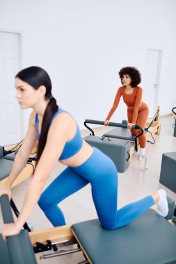 İki kadın, parlak bir stüdyoda yenilikçi makineler kullanarak dinamik bir pilates çalışmasına girişiyor..