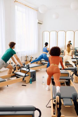 Katılımcılar iyi aydınlatılmış bir stüdyoda pilates egzersizlerine konsantre oluyorlar..