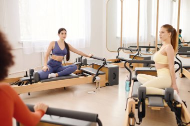 İki kadın esneyip sakin bir stüdyo ortamında pilates rutinlerine odaklanıyorlar..