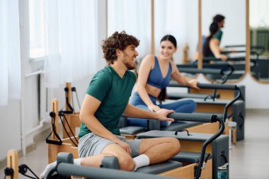 İki sporcu, parlak bir stüdyoda pilates yapmaya hazırlanırken keyifli bir anı paylaşıyorlar..