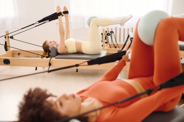 İki kadın reformcularla pilates yapıyor. Güneşli bir stüdyoda dayanıklılık ve esnekliği arttırıyor..