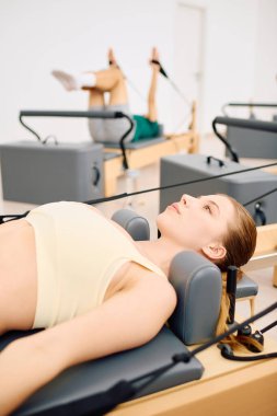 Bir kadın bir reformcu üzerinde pilates yaparken, diğer bir katılımcı yakınlarda geriliyor..