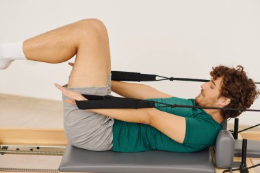 Parlak bir stüdyoda çekirdek kuvvet ve esneklik oluşturmak için dinamik bir pilates çalışması yapan bir adam..