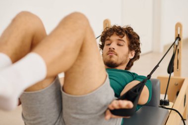 Genç bir adam pilates yapıyor, dayanıklılık ve esnekliği geliştirmek için özel ekipmanlar kullanıyor..