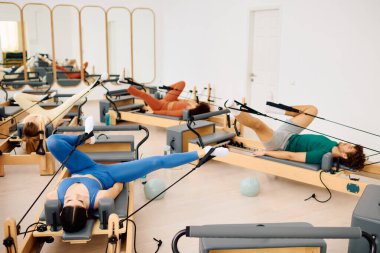 Bir grup birey, iyi aydınlatılmış bir stüdyo ortamında senkronize pilates egzersizleri yapıyor.