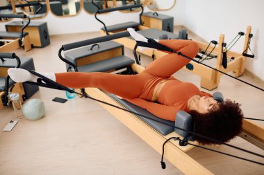 Çekirdek kaslarını güçlendirmeye odaklanan bir kadın, iyi donanımlı bir stüdyoda pilates yapıyor..