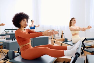 Katılımcılar parlak bir alanda çekirdek kuvveti ve esnekliğine odaklanan pilates egzersizleri yapıyorlar.