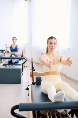 İki birey parlak bir stüdyoda pilates yapıyor, güçlerini ve esnekliklerini arttırıyor..
