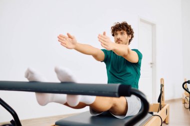 Bir adam, parlak, geniş bir pilates stüdyosunda bir reformcu üzerinde kontrollü hareketler yapıyor..