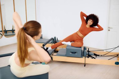 İki birey pilates egzersizi yapıyor, stüdyoda form ve işbirliği gösteriyorlar..