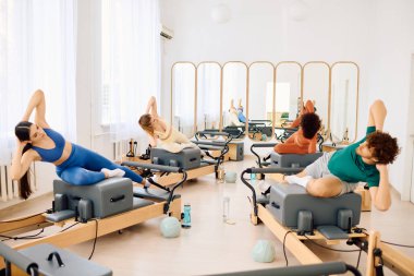 Katılımcılar hareketli bir pilates dersi sırasında reformcuları kullanırken tekniklerine odaklanıyorlar.