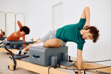 Parlak bir stüdyoda özel ekipman kullanarak iki kişi çeşitli pilates teknikleri uyguluyor..