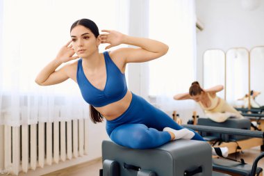 Kendini işine adamış iki kişi, parlak ve havadar bir stüdyoda doğal ışıkla pilates egzersizleri yapıyorlar..