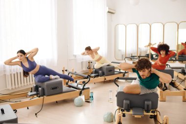 Katılımcılar canlı bir ders sırasında özel ekipman kullanarak yoğun pilates egzersizleri yapıyorlar.