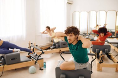 Katılımcılar, parlak ve havadar bir stüdyoda pilates rutinlerine dalıyorlar..